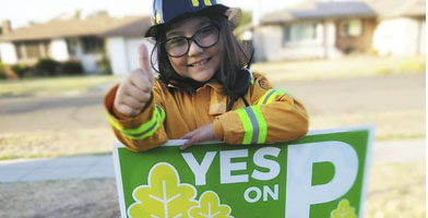 A child giving a "thumbs up" over a sign saying "Yes on P".