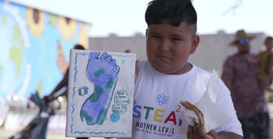 A boy holding a small canvas with a painting of a foot.