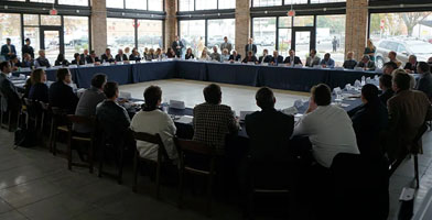 A group of people, at a conference, sitting at a big square table.